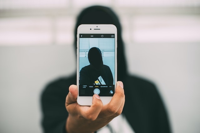 Hooded person taking a picture of himself with the phone.